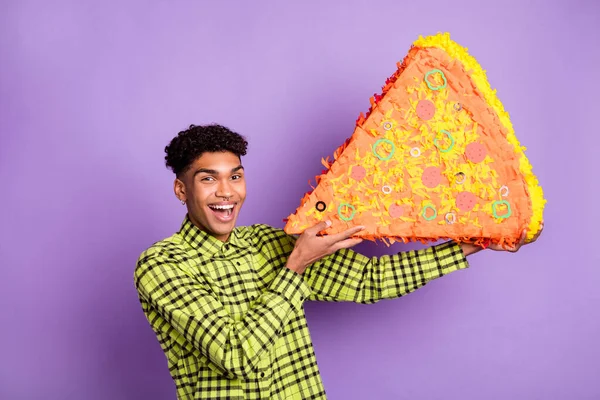 Retrato de buen chico morena alegre sosteniendo en las manos comiendo pedazo de pizza grande artificial aislado sobre violeta color púrpura fondo —  Fotos de Stock