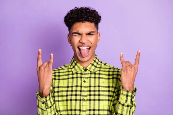 Foto de loco de piel oscura joven mostrar signos con cuernos sobresalen lengua aislada en el fondo de color púrpura —  Fotos de Stock