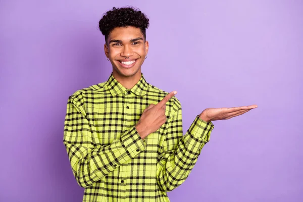 Ritratto di attraente ragazzo dai capelli ondulati allegro che tiene su palmo dimostrando spazio copia isolato su sfondo viola viola — Foto Stock