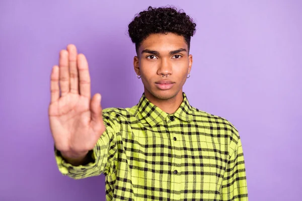 Foto de piel oscura grave joven sostener la mano mostrar señal de stop negar aislado en el fondo de color violeta —  Fotos de Stock