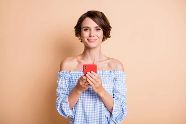 Foto retrato de una mujer sonriente sosteniendo el teléfono en dos manos aisladas sobre fondo de color beige pastel —  Fotos de Stock