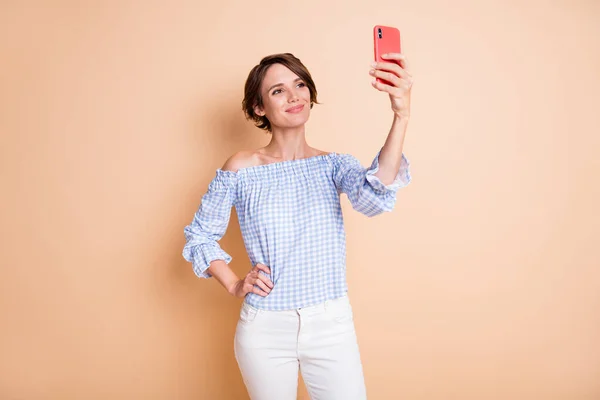 Gülümseyen bir kadının fotoğrafı. Bir elinde selfie tutan bir kadın. Pastel bej renkli arka planda izole edilmiş. — Stok fotoğraf
