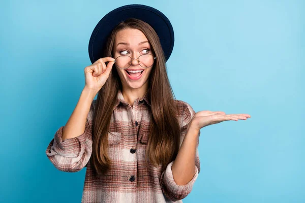 Foto de joven feliz emocionado loco sonriente joven publicidad producto gafas sombrero aislado sobre fondo de color azul —  Fotos de Stock