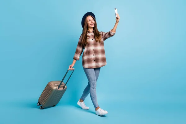 Полноразмерная фотография улыбающейся девушки, путешествующей с рюкзаком, сделайте селфи на телефоне, изолированном на синем цветовом фоне — стоковое фото