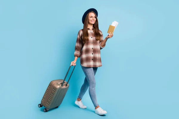 Pełnowymiarowe zdjęcie młodej wesołej uśmiechniętej atrakcyjnej dziewczyny iść z bagażem i bilety wyglądają copyspace izolowane na tle niebieskiego koloru — Zdjęcie stockowe