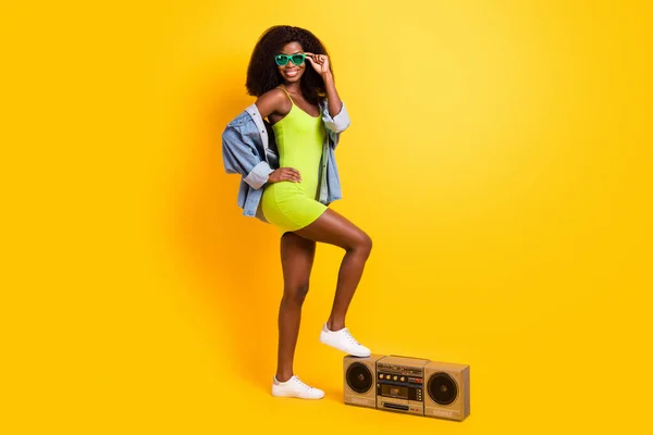 Teljes méretű fotó fiatal mosolygós hűvös magabiztos afro lány fel láb boombox elszigetelt sárga színű háttér — Stock Fotó