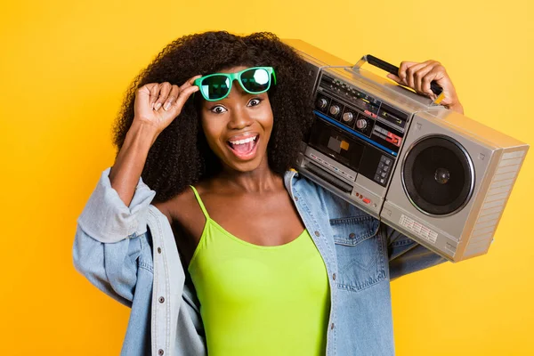 Zdjęcie młodego, pięknego, uśmiechniętego hipstera afro dziewczyny z boomboxem na ramionach odizolowanego na żółtym tle — Zdjęcie stockowe