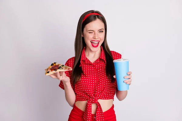 照片上滑稽可爱的女孩拿着比萨饼片捧着杯子苏打水眨眼穿上红点衬衫孤立的灰色背景 — 图库照片