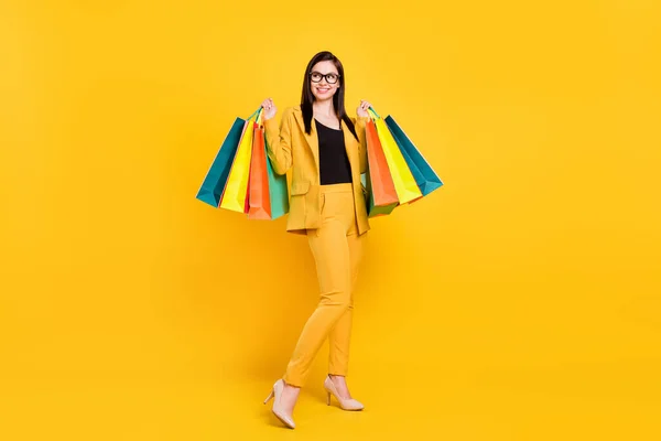 Foto de cuerpo completo de dulce joven dama mantenga bolsas mirada espacio vacío desgaste gafas traje amarillo aislado sobre fondo de color vivo —  Fotos de Stock