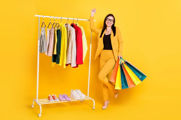 Pełny rozmiar zdjęcie hura młoda dama trzymać torby w pobliżu garderobe nosić okulary żółty garnitur izolowane na żywe tło kolor — Zdjęcie stockowe
