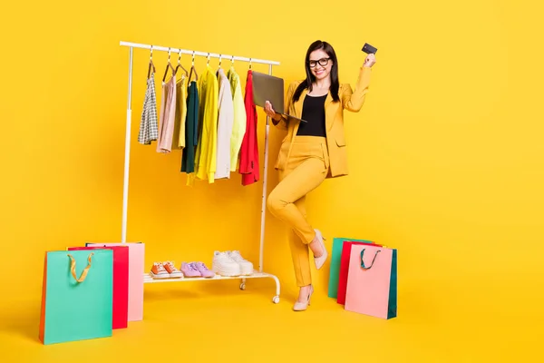 Full size zdjęcie młodej kobiety szczęśliwy uśmiech sklep online laptop zapłacić karty kredytowe szafa torby sprzedaż izolowane na żółtym tle — Zdjęcie stockowe