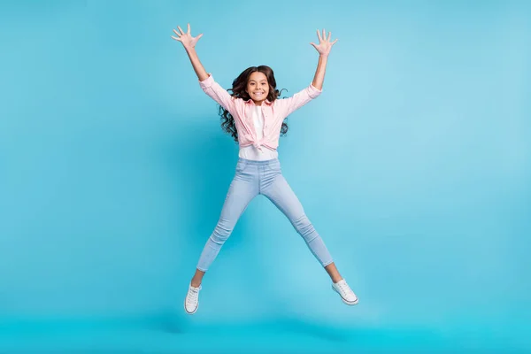 Ganzkörperporträt von unbeschwerten Schulmädchen springen heben Hände haben Spaß isoliert auf blauem Hintergrund — Stockfoto