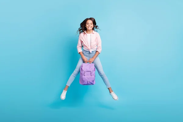 Фотографія повного розміру молодого веселого гарного настрою позитивна дівчина стрибає тримайте фіолетовий рюкзак ізольовано на синьому кольорі — стокове фото