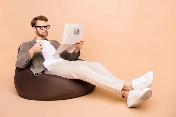 Pleine taille photo de sérieux concentré jeune homme assis chaise lire papier boisson café isolé sur fond de couleur beige — Photo