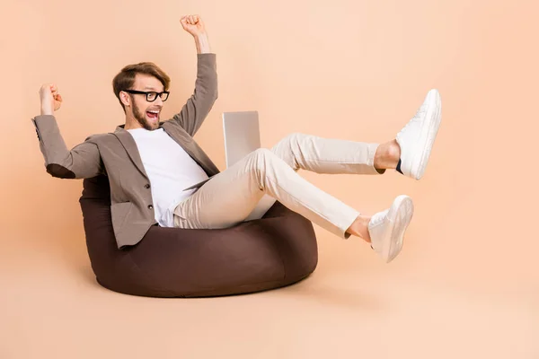 Foto de tamaño completo de feliz empresario loco emocionado en gafas levantar los puños en el uso de la victoria portátil aislado sobre fondo de color beige — Foto de Stock