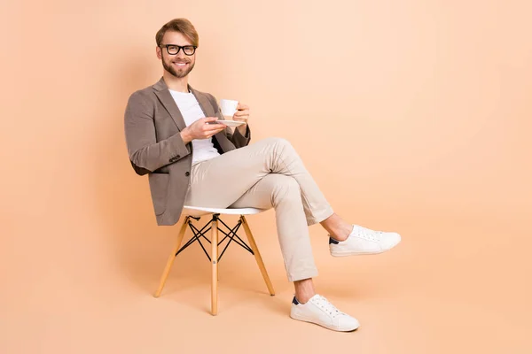 Full size foto van gelukkig knappe aantrekkelijke charismatische man in glazen ontspannen drinken thee geïsoleerd op beige kleur achtergrond — Stockfoto