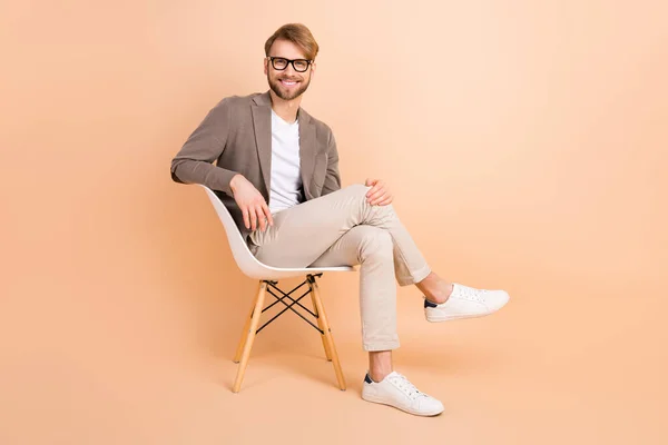 Volledige grootte foto van aantrekkelijke charismatische heer in bril zitten stoel pauze pauze ontspannen geïsoleerd op beige kleur achtergrond — Stockfoto