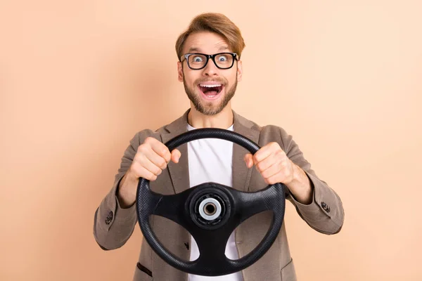 Foto de feliz animado bom humor louco empresário montando carro segurar volante isolado no fundo cor bege — Fotografia de Stock