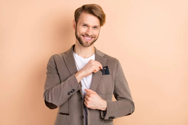 Foto de optimista pelo rubio agradable hombre llevan tarjeta de uso chaqueta gris aislado sobre fondo beige — Foto de Stock