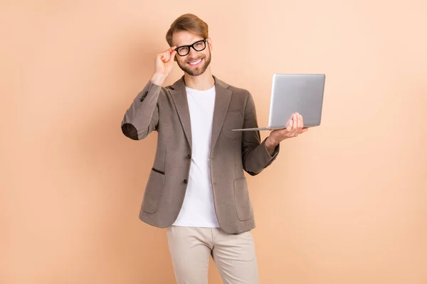 Foto de otimista agradável cabelo loiro homem segurar laptop desgaste óculos casaco cinza isolado no fundo bege — Fotografia de Stock