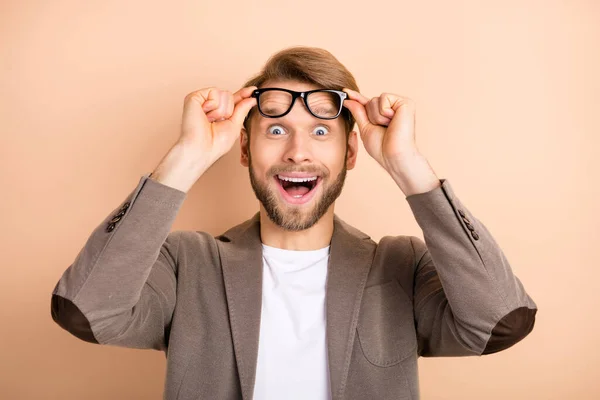 Foto van aantrekkelijke opgewonden jonge man dragen jas armen bril grote ogen open mond geïsoleerde beige kleur achtergrond — Stockfoto