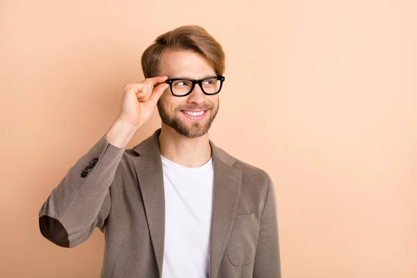 Foto van zelfverzekerde aantrekkelijke jonge man dragen jas arm bril op zoek lege ruimte geïsoleerde beige kleur achtergrond — Stockfoto