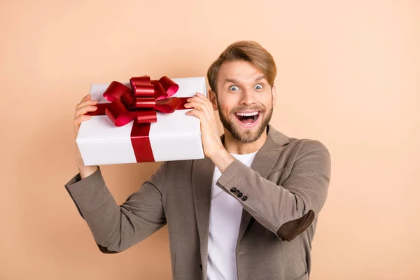 Foto de divertido chico joven excitado usar chaqueta sonriente adivinando lo que dentro de la caja de regalo aislado color beige fondo —  Fotos de Stock