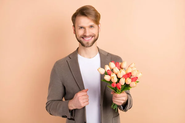 Photo of cute classy young guy wear jacket smiling holding big tulips bouquet isolated beige color background — Stock Photo, Image