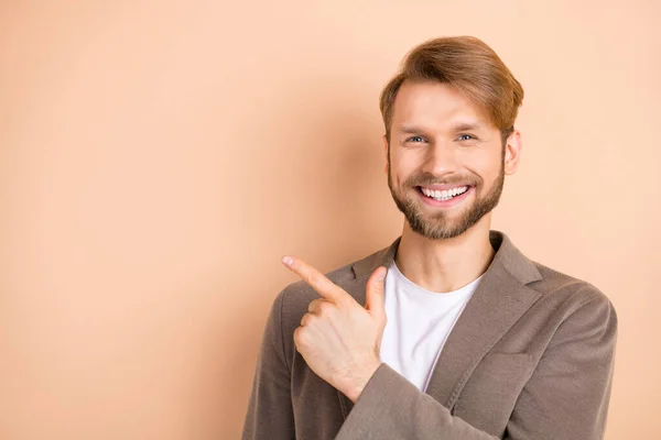 Foto de confiante adorável jovem desgaste casaco sorrindo apontando espaço vazio isolado cor bege fundo — Fotografia de Stock