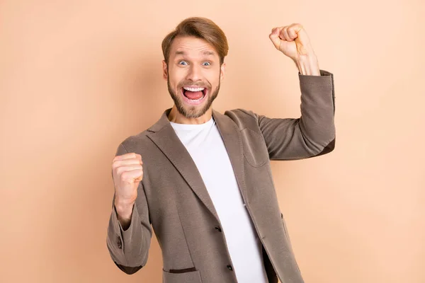 Foto van opgewonden gelukkige jonge man dragen jas glimlachende rijzende vuisten geïsoleerde beige kleur achtergrond — Stockfoto