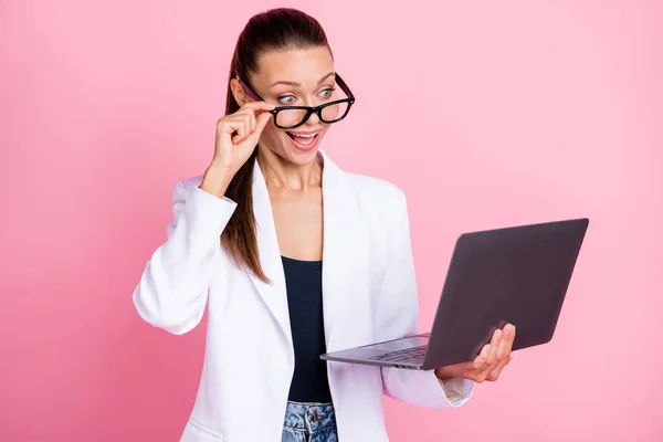 Photo de jeune femme excitée étonnée tenir des lunettes d'ordinateur portable nouvelles inattendues isolé sur fond rose pastel — Photo