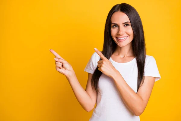 Retrato fotográfico de una mujer vestida con una camiseta blanca que muestra el espacio en blanco del dedo aislado sobre un vibrante fondo de color amarillo —  Fotos de Stock