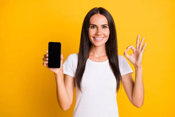 Foto porträtt av kvinnliga student visar mobiltelefon display copyspace visar okej tecken isolerad på ljusgul färg bakgrund — Stockfoto