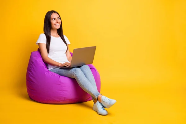 Foto wanita muda mengkilap mengenakan t-shirt putih duduk beanbag mengetik gadget modern mencari ruang kosong warna kuning latar belakang yang terisolasi — Stok Foto