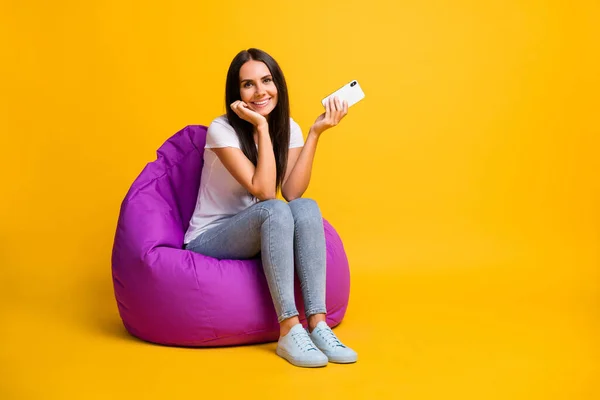 Foto de mulher encantadora vestida branco t-shirt sentado feijão saco segurando moderno dispositivo vazio espaço isolado cor amarela fundo — Fotografia de Stock