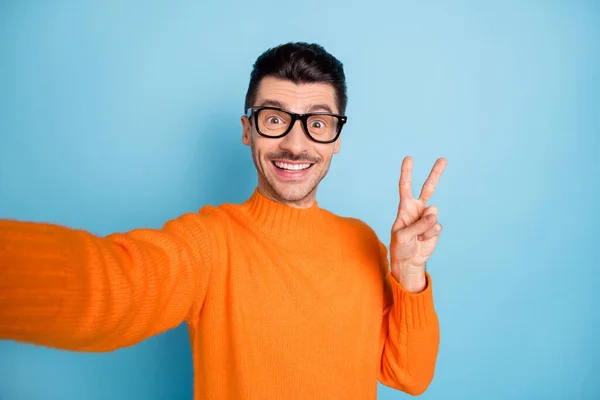 Genç adamın mutlu gülümsemesinin fotoğrafı selfie 'nin mavi arka planda izole edilmiş güzel bir v-işareti göstermesini sağlar. — Stok fotoğraf