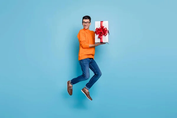 Портрет повного тіла веселого красивого людини, що стрибає, тримає подарункову коробку зубну посмішку ізольовану на синьому кольорі — стокове фото