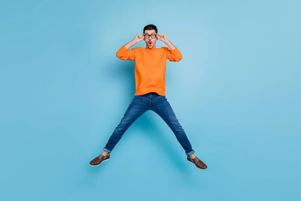 Полноразмерный портрет шокированного молодого человека, прыгающего с открытым ртом и смотрящего на руки в очках, изолированных на синем фоне — стоковое фото