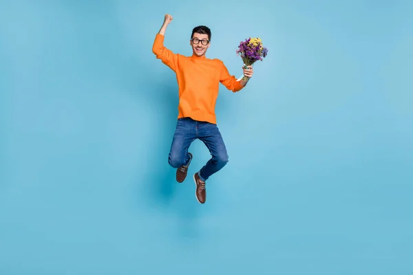 フルサイズ写真の驚くべきハンサムな男ジャンプ拳アップホールド花で隔離された青の色の背景 — ストック写真