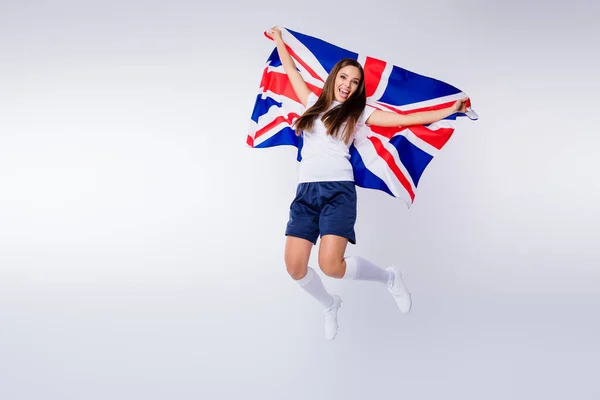 Foto de longitud completa positivo chica energética ventilador de fútbol disfrutar de apoyo campeonato de la Copa del Mundo equipo nacional grito salto mantenga bandera del Reino Unido usar camiseta pantalones cortos calcetines aislados color gris fondo —  Fotos de Stock