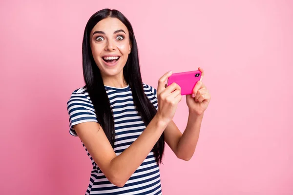 Fotoporträt von erstaunt Mädchen mit offenem Mund hält Telefon in zwei Händen vertikal isoliert auf pastellrosa farbigem Hintergrund — Stockfoto