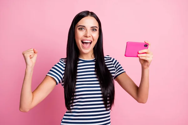 Fénykép portré lány ünneplő emelt ököllel tartó telefon egyik kezében függőlegesen elszigetelt pasztell rózsaszín színű háttér — Stock Fotó