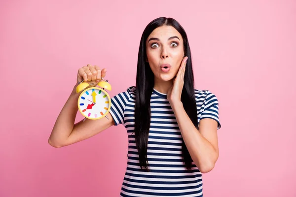 Retrato fotográfico de una mujer conmocionada tocando la cara de la mejilla sosteniendo el reloj amarillo en una mano aislada sobre fondo de color rosa pastel —  Fotos de Stock