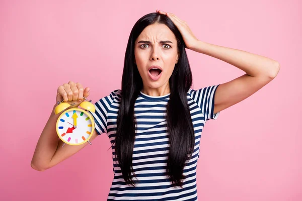 Photo portrait of unhappy gasping girl touching head holding yellow clock in one hand isolated on pastel pink colored background — Stock Photo, Image