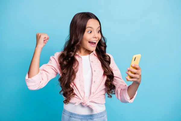 Foto de jovem feliz positivo animado louco menina levantar punho na vitória usando smartphone isolado no fundo de cor azul — Fotografia de Stock