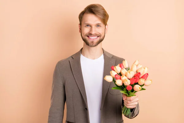 Foto de bastante lindo joven usar chaqueta sonriente celebración de grandes tulipanes ramo aislado color beige fondo — Foto de Stock