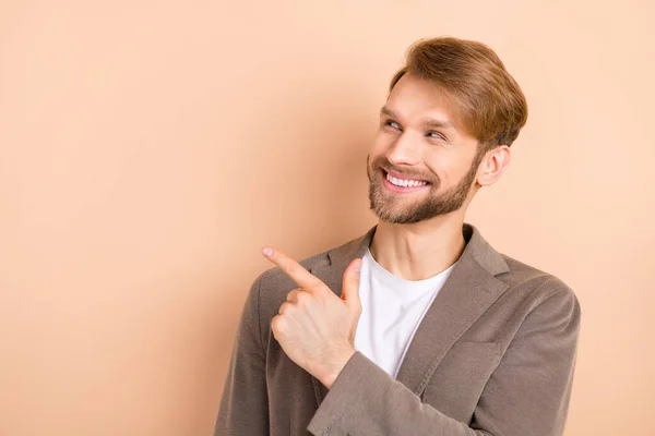 Foto av rolig söt ung gentleman klädd kavaj ser pekar tomt utrymme leende isolerad beige färg bakgrund — Stockfoto