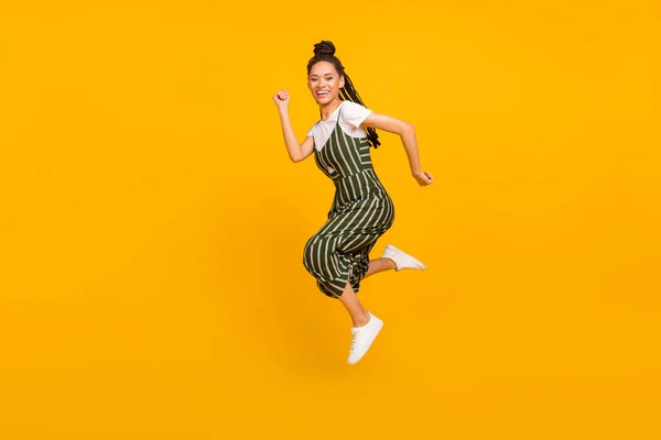 Foto de longitud completa de la divertida mujer de piel oscura dulce vestido traje a rayas sonriendo saltando alto aislado color amarillo fondo — Foto de Stock