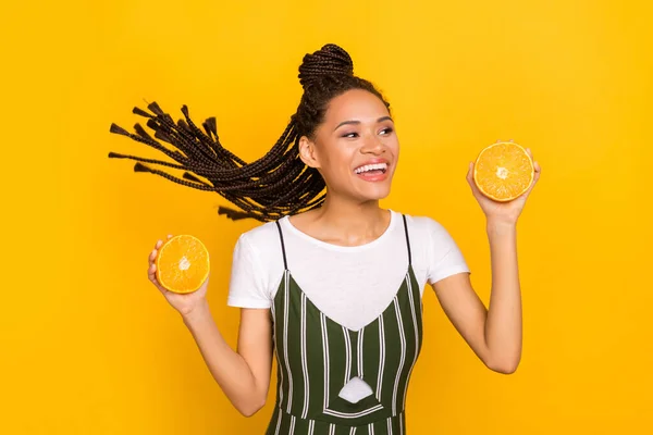 Retrato de menina alegre atraente se divertindo segurando em mãos pedaços de laranja isolados sobre fundo de cor amarelo brilhante — Fotografia de Stock
