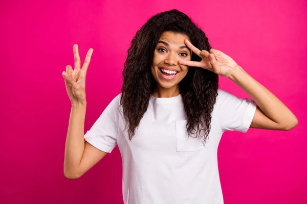 Foto di pazza bruna ondulato giovane signora mostra v-segno indossare bianco t-shirt isolato su sfondo di colore rosa vivido — Foto Stock